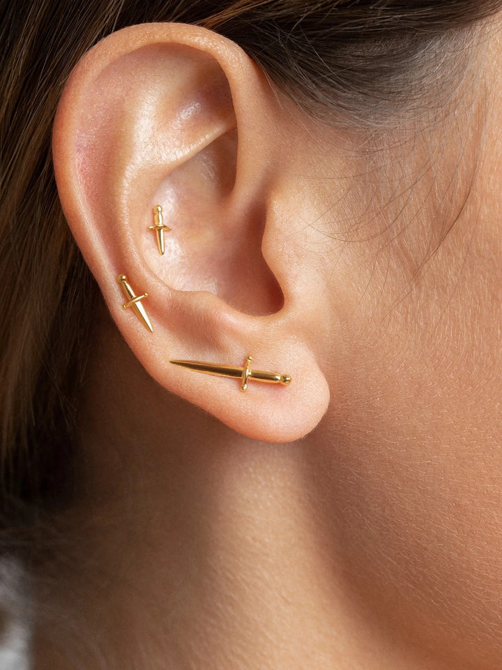 Cartilage earring with small gold dagger, styled on upper ear for a refined yet edgy look.