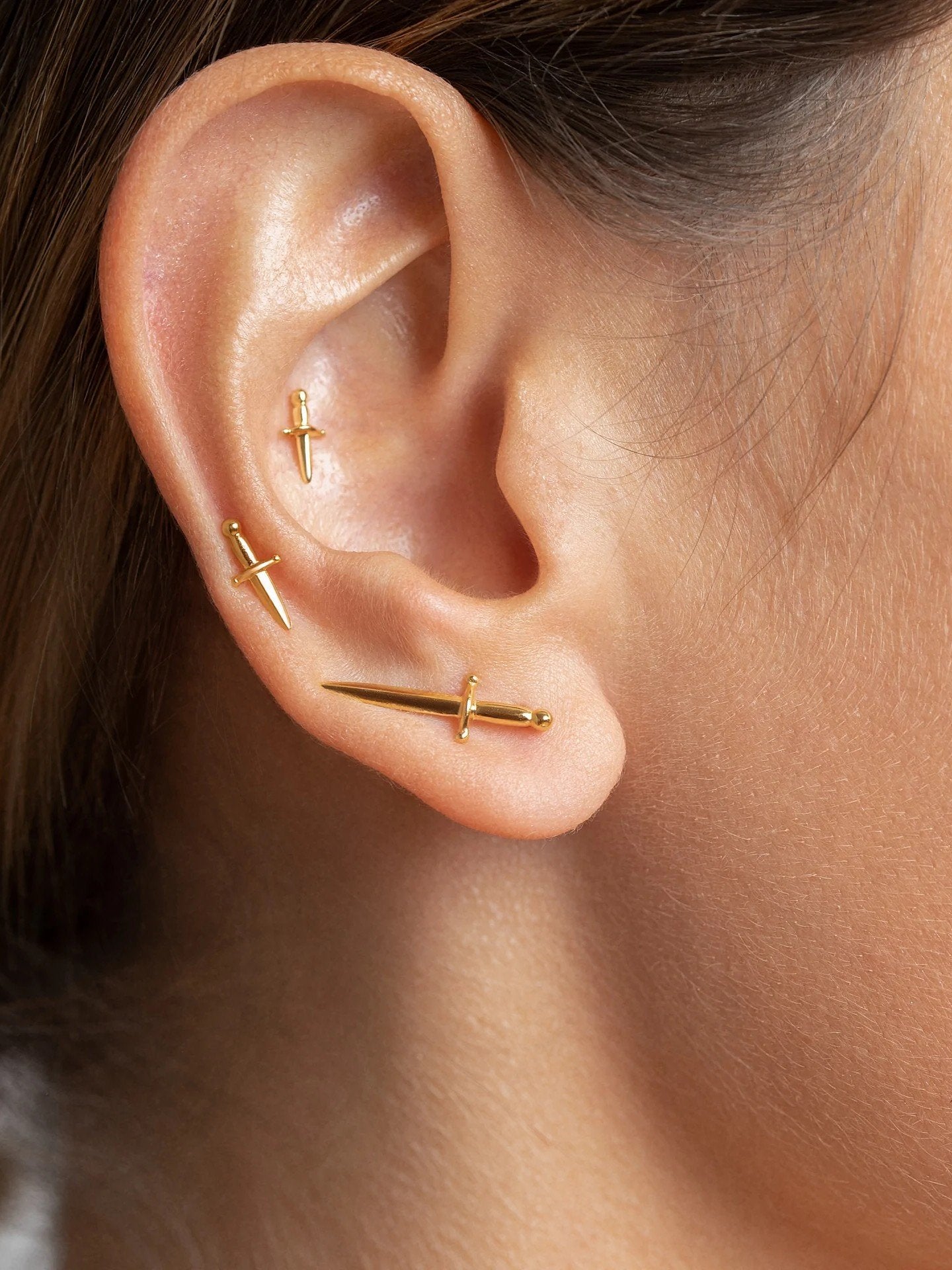 Cartilage earring with small gold dagger, styled on upper ear for a refined yet edgy look.