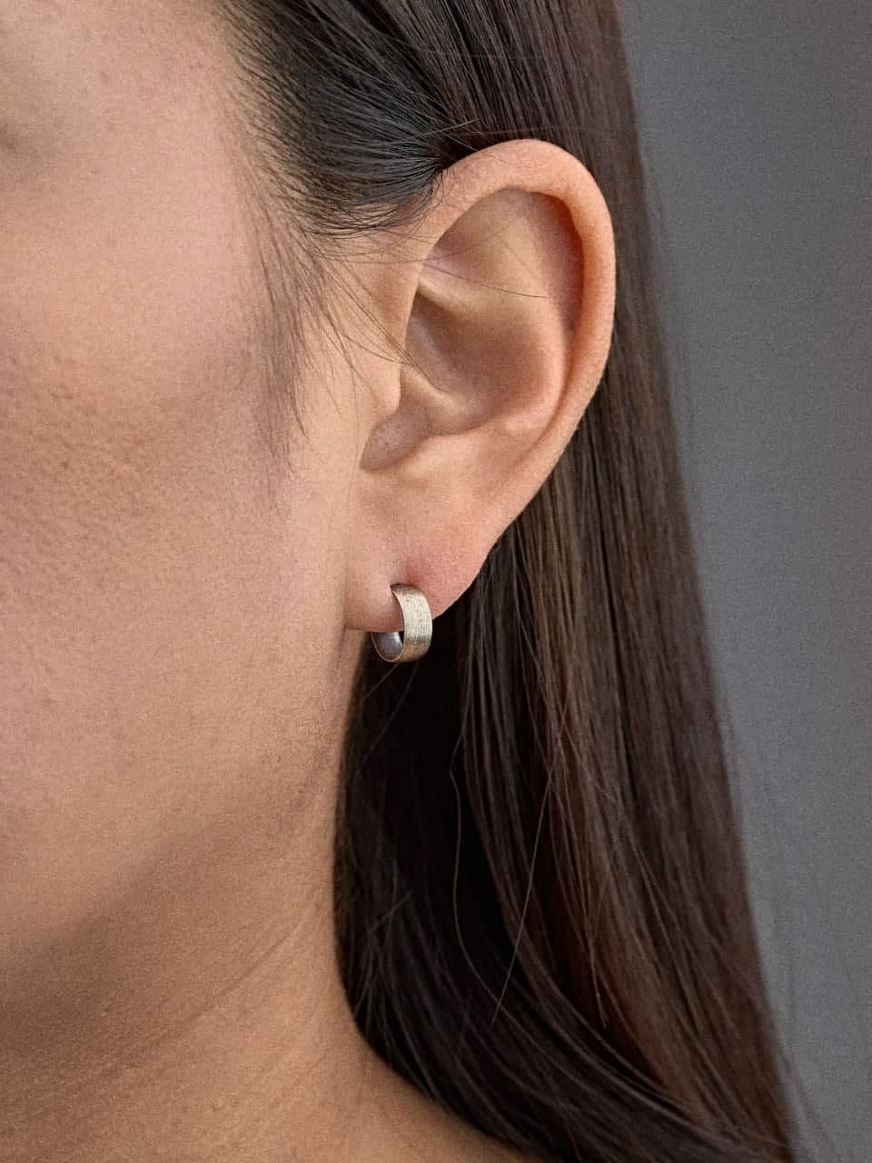 Petite sterling silver hoop earring worn on earlobe, side view of model.