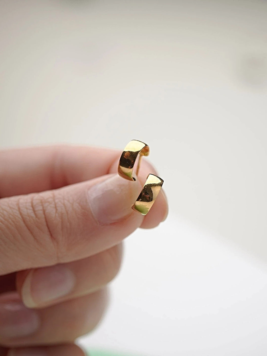 Close-up of gold-plated hoop earring held between fingers.