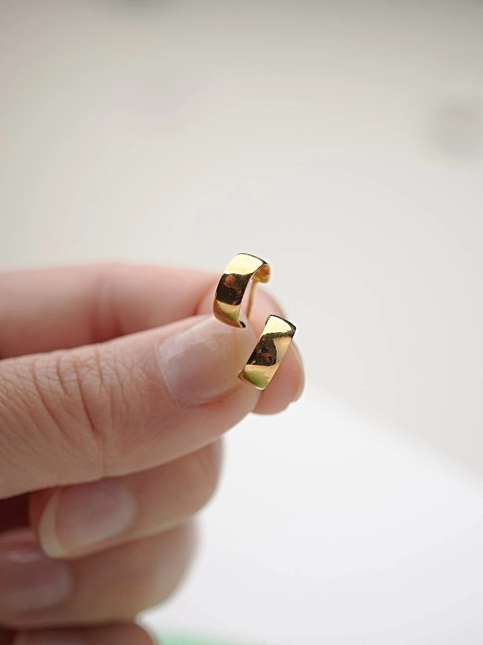 Close-up of gold-plated hoop earring held between fingers.