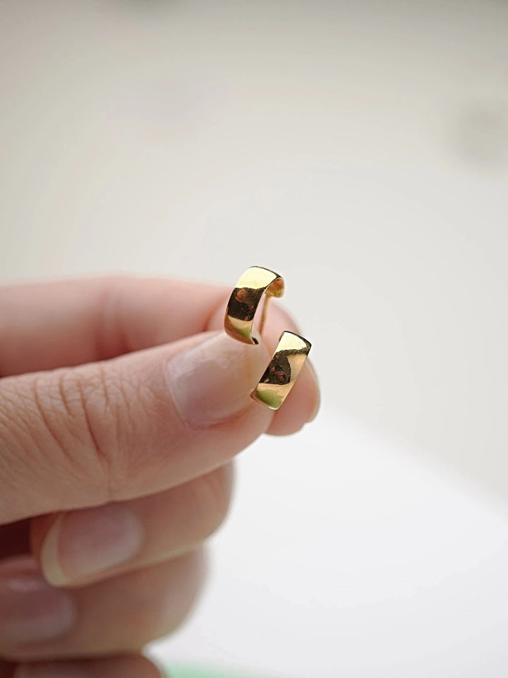 Close-up of gold-plated hoop earring held between fingers.