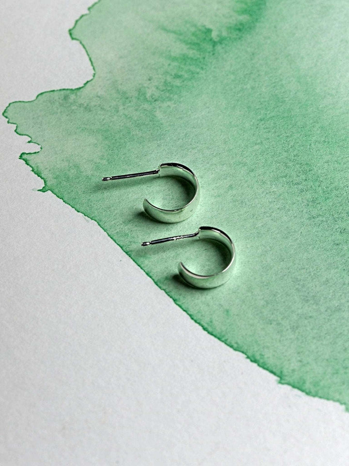 Minimalist sterling silver hoop earrings flat-lay on watercolor green paper.