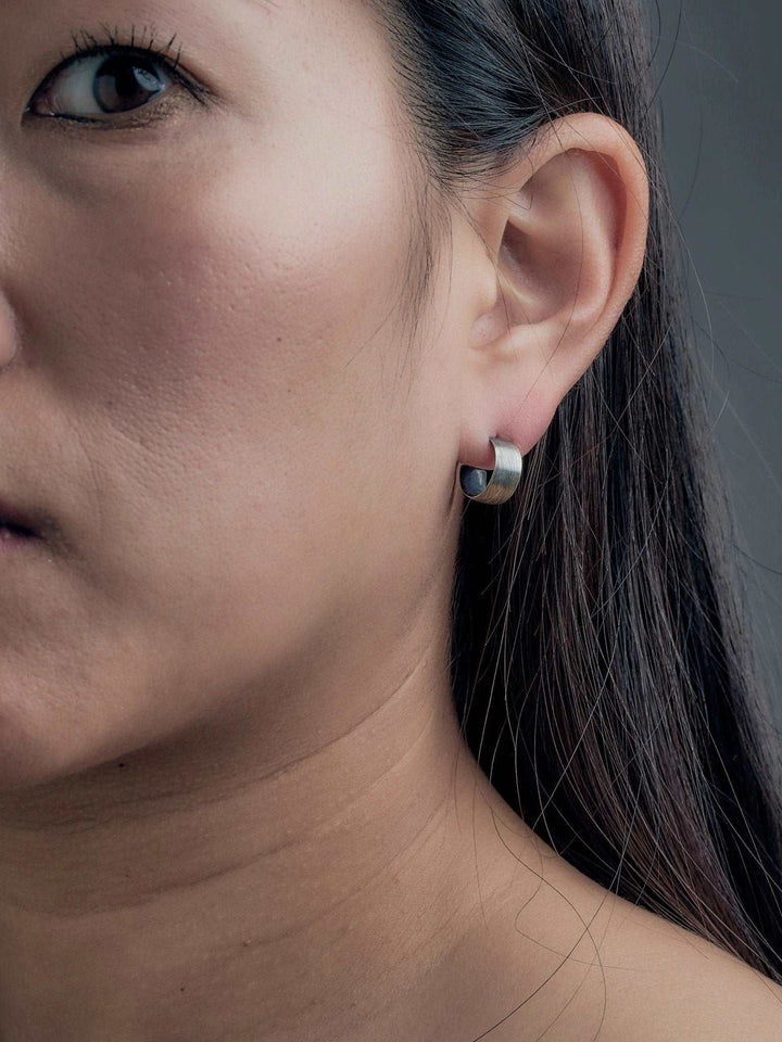 Oxidized silver hoop earring worn on earlobe, side view of woman with straight hair.