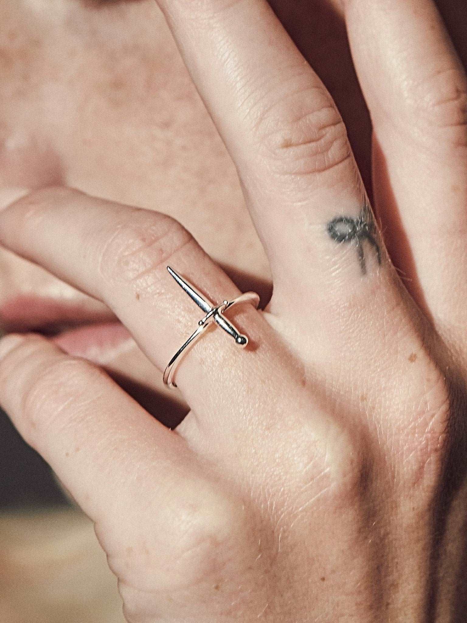 Sterling Silver dagger ring on hand with warm lighting and layered rings.