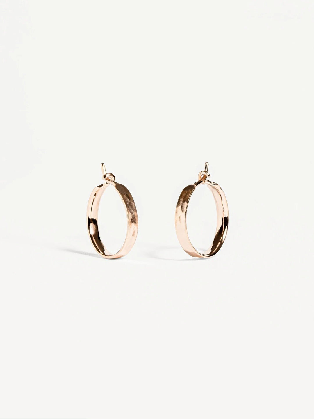 Nanna huggie hoop earrings in matte rose gold plated finish — hammered texture on soft white background.