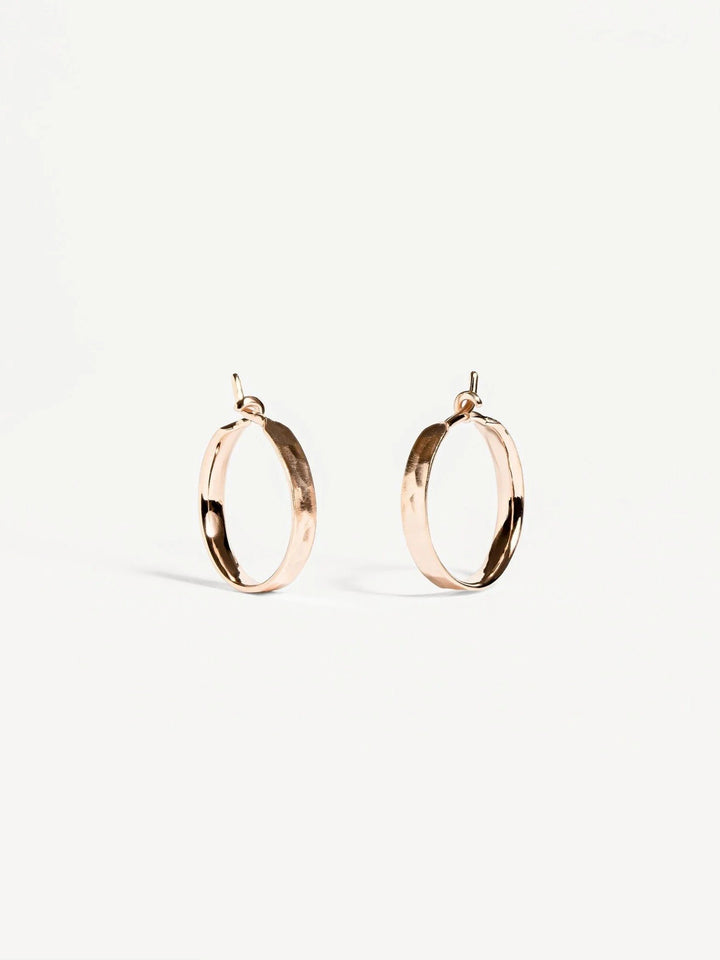 Nanna huggie hoop earrings in matte rose gold plated finish — hammered texture on soft white background.
