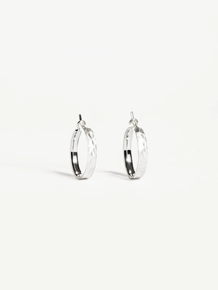 Nanna huggie hoops in matte sterling silver — hammered surface with minimalist style.