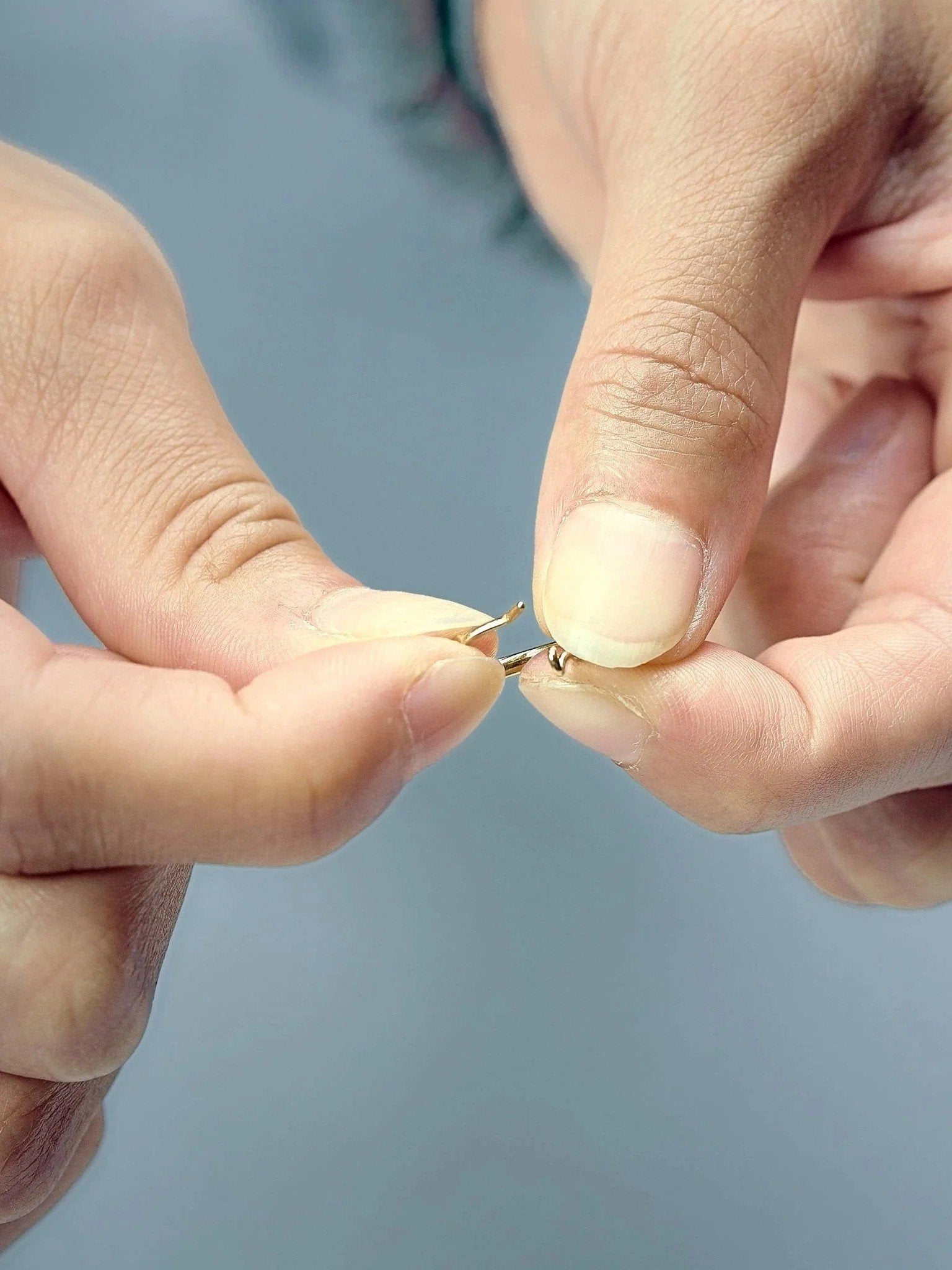 Nanna huggie hoop earring in matte gold finish — shown being gently opened to demonstrate secure clasp mechanism.