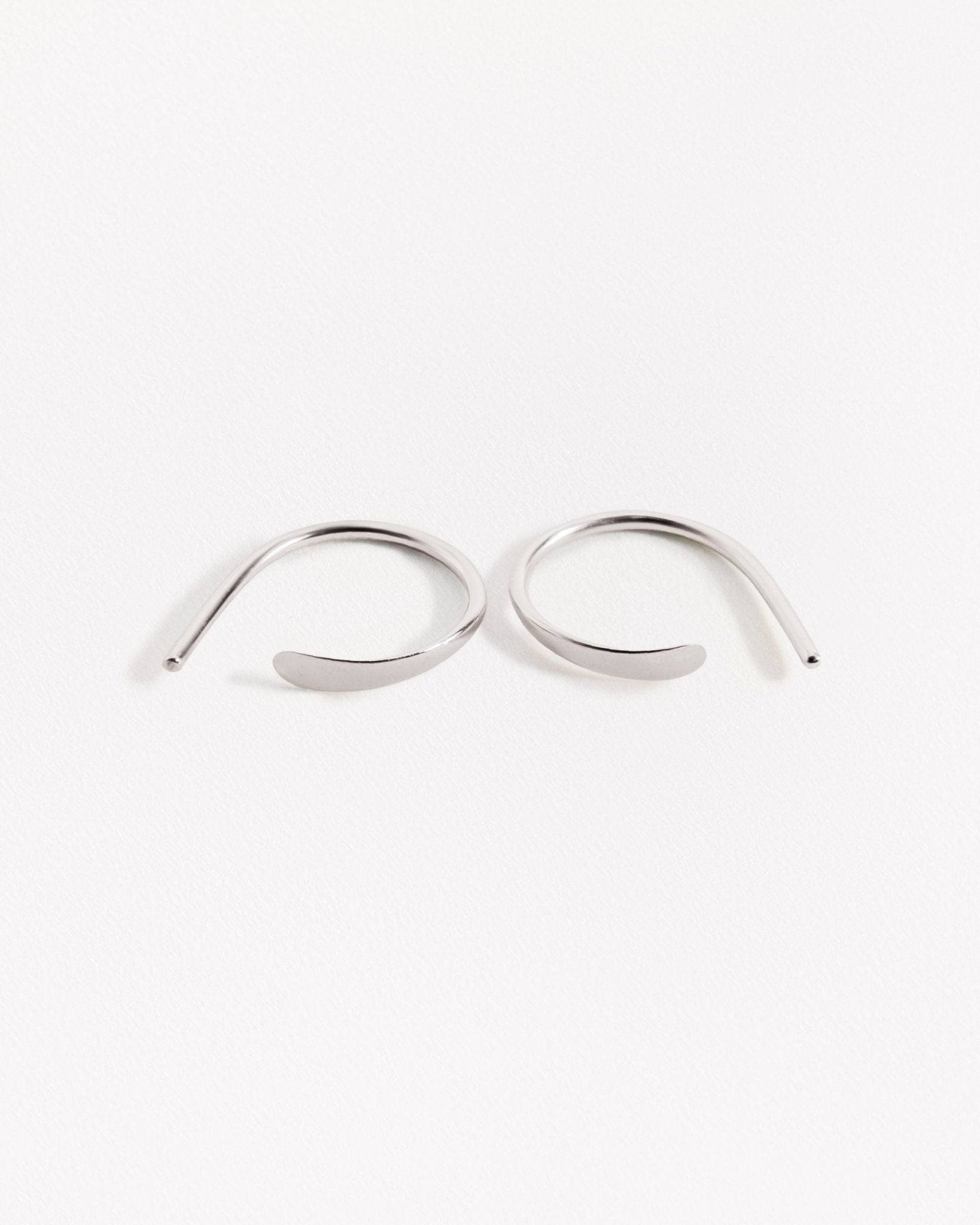Noe hammered hoops in silver finish — gracefully curved pair with polished shine on white background.