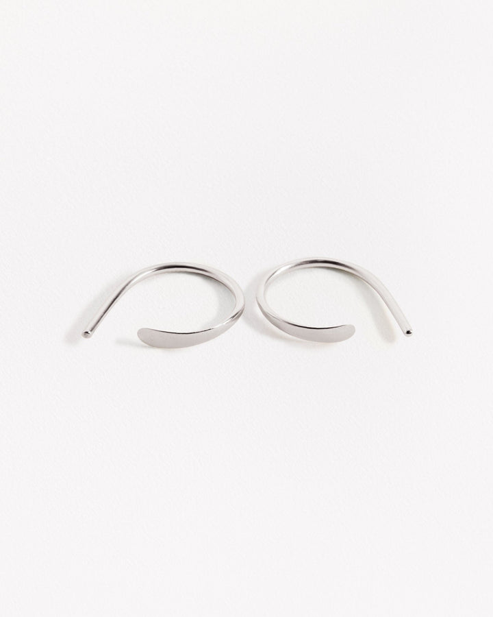 Noe hammered hoops in silver finish — gracefully curved pair with polished shine on white background.