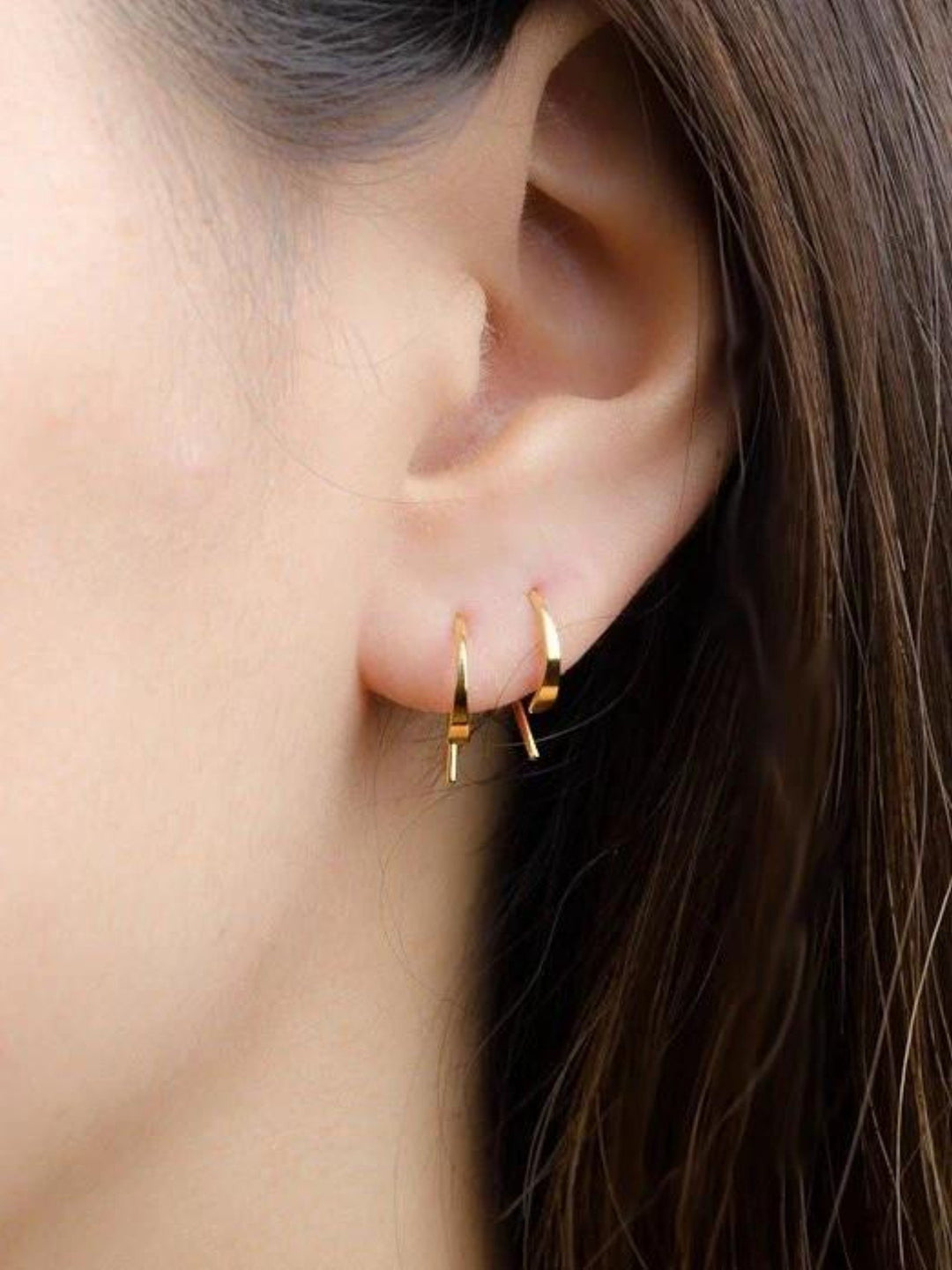 Gold Noe hammered hoop earring stacked with other minimalist earrings — shown worn on ea