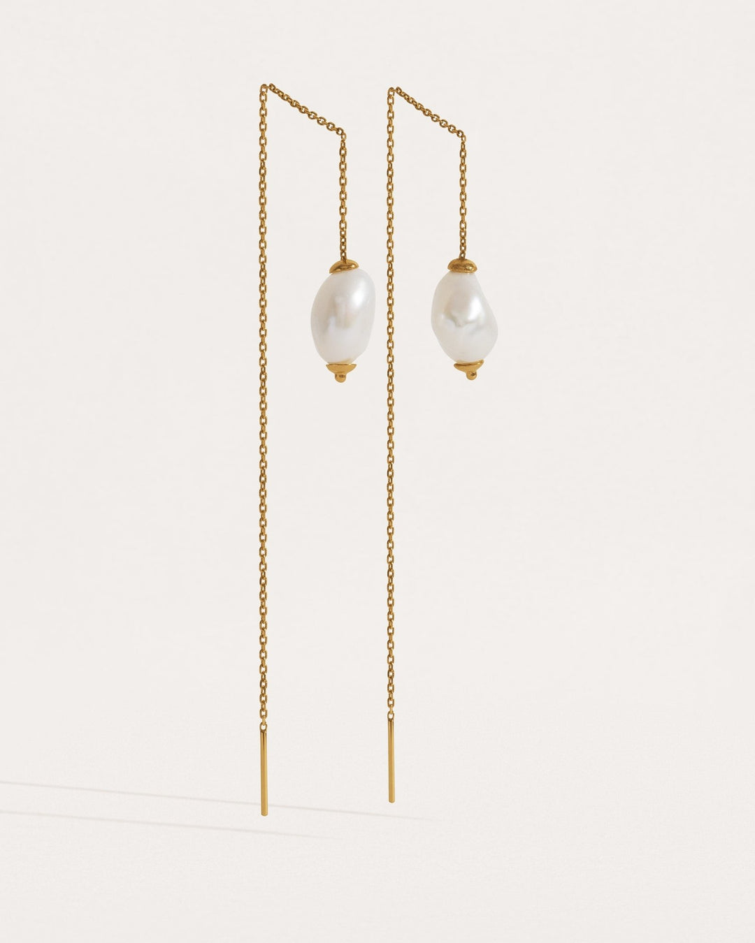 Two pairs of threader earrings in silver and gold finishes — freshwater pearl drops on fine chain.