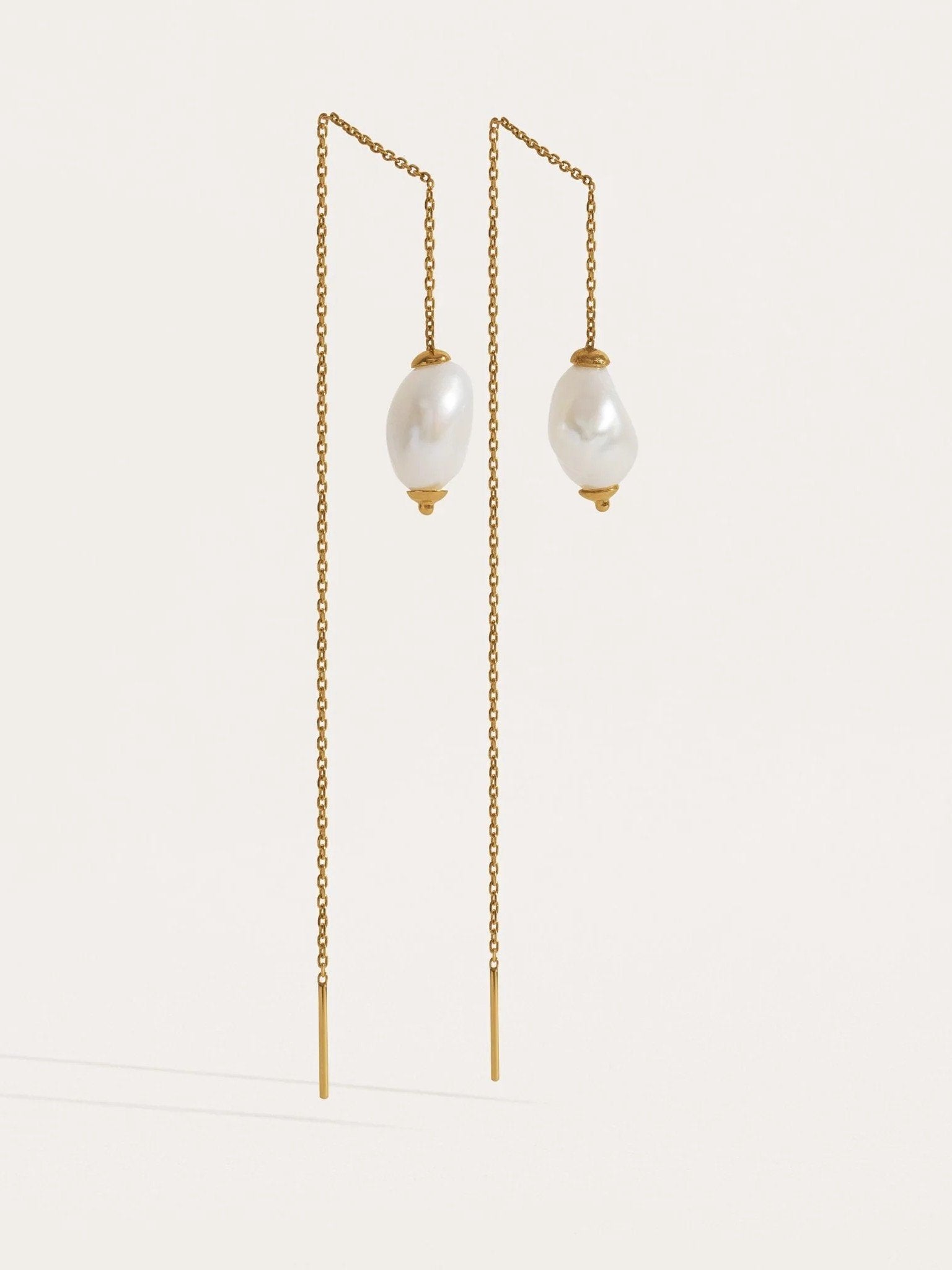 Two pairs of threader earrings in silver and gold finishes — freshwater pearl drops on fine chain.