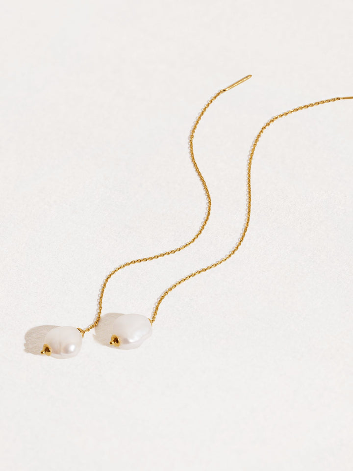Curved display of gold threader earrings with natural pearl drops — graceful minimalist styling.
