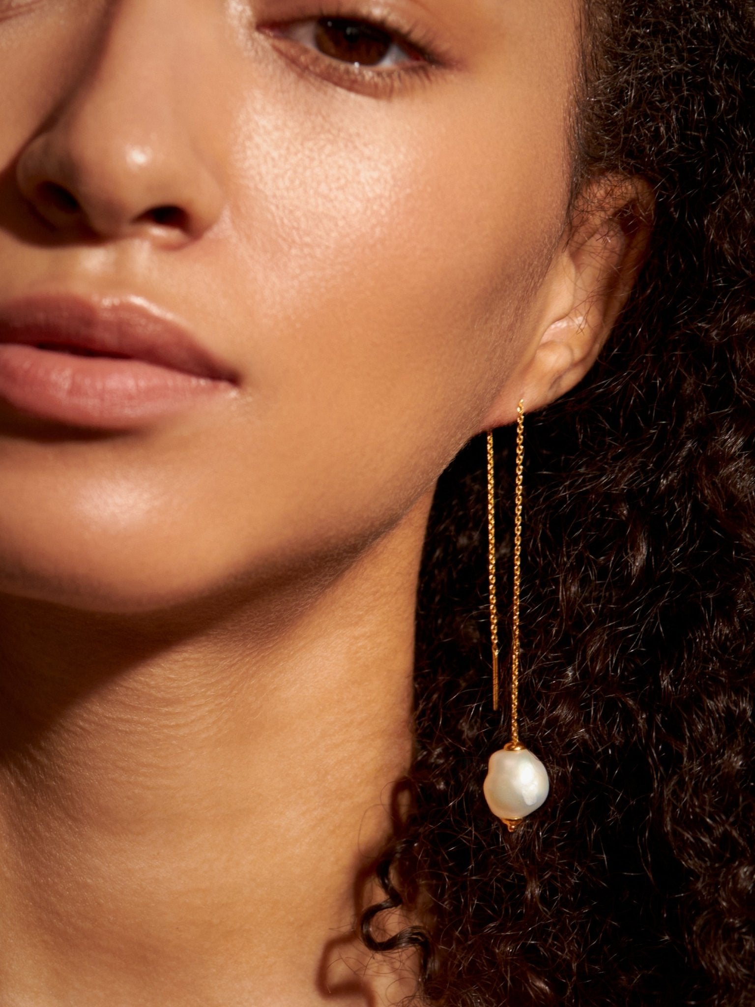 Close-up of gold threader pearl earring worn — elegant curve and soft shine captured on skin.