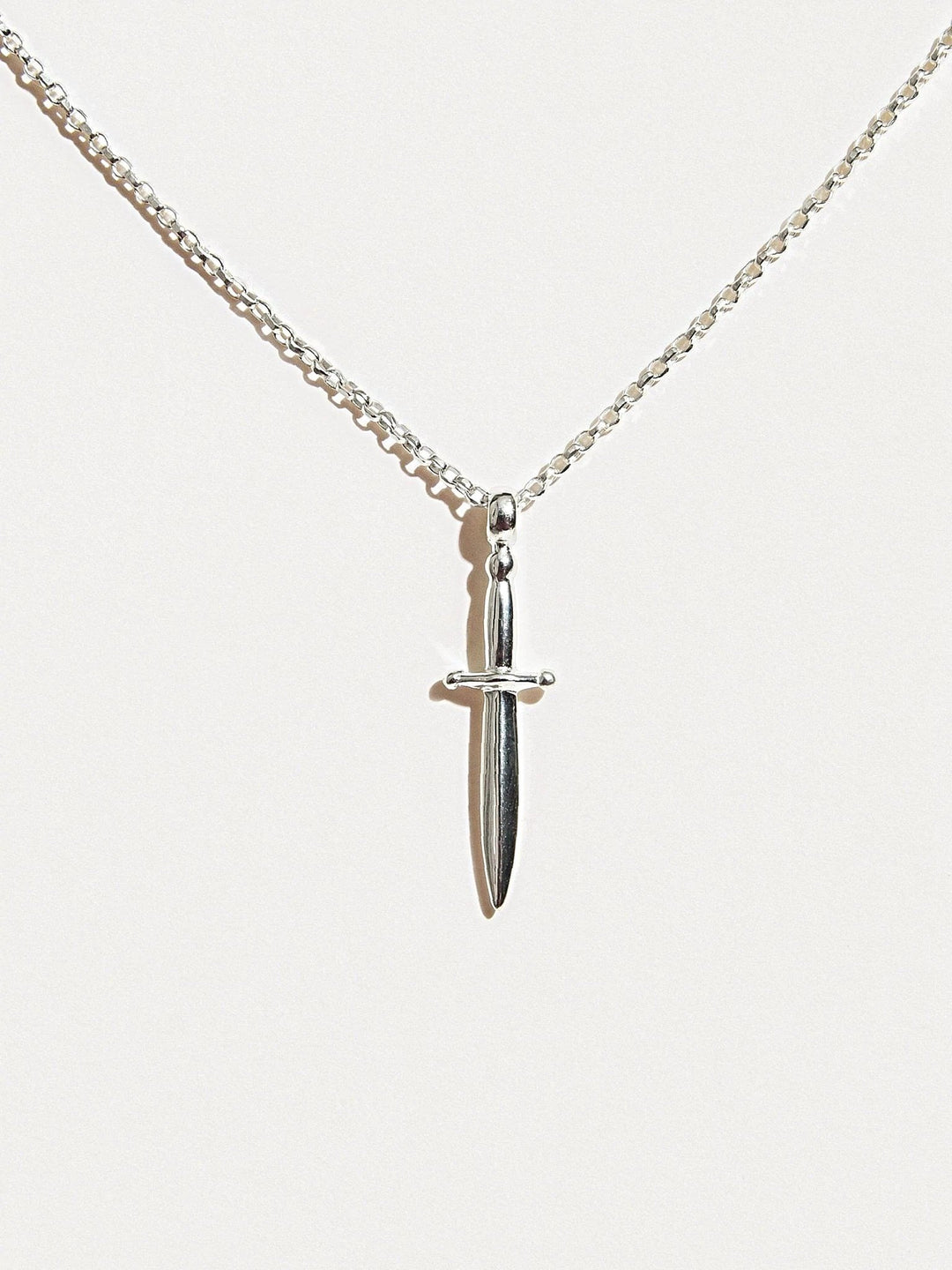 Sterling silver dagger necklace hanging on white background, clean full view.
