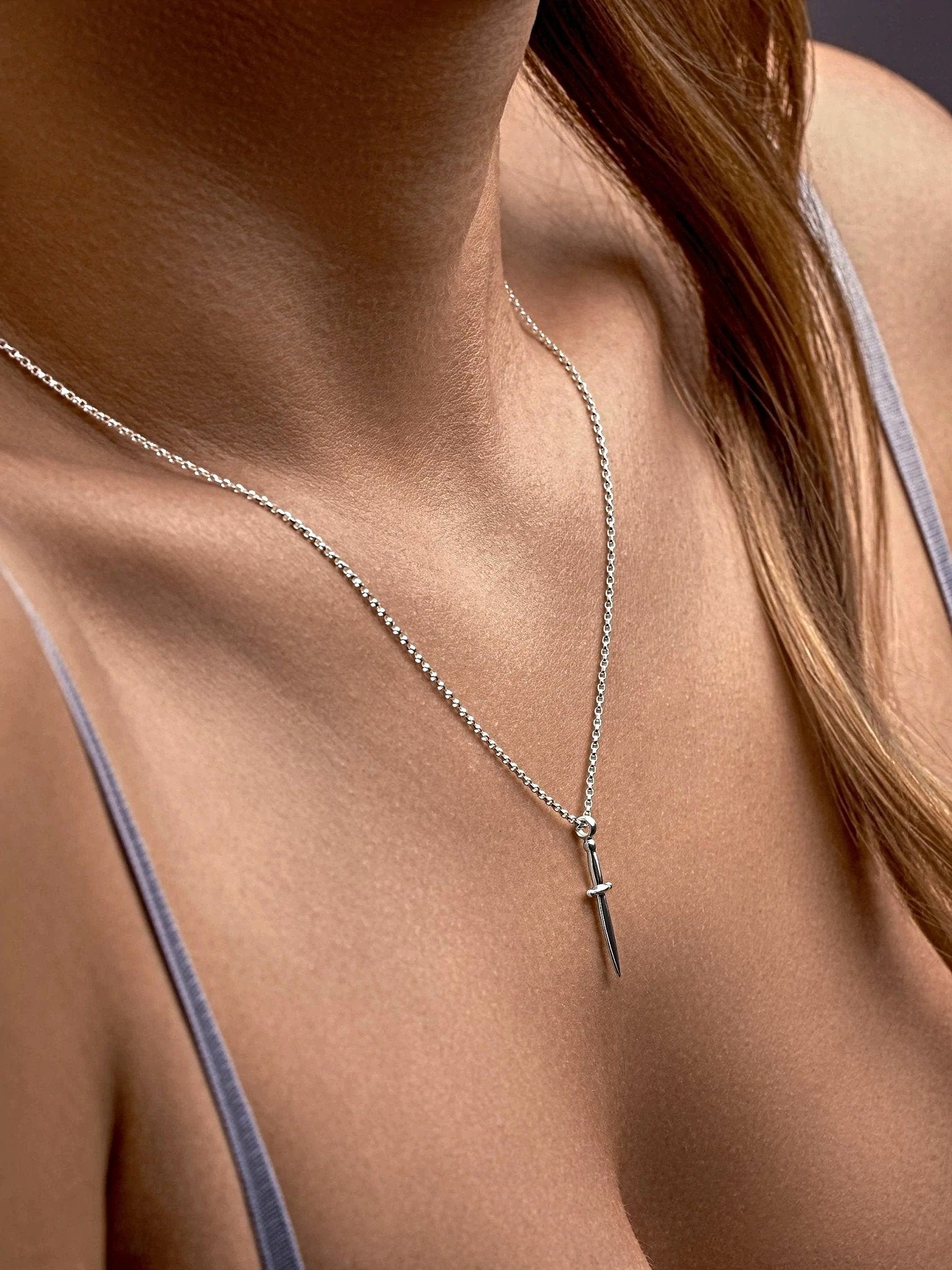 Silver dagger necklace styled on deep neckline with warm shadowed lighting.