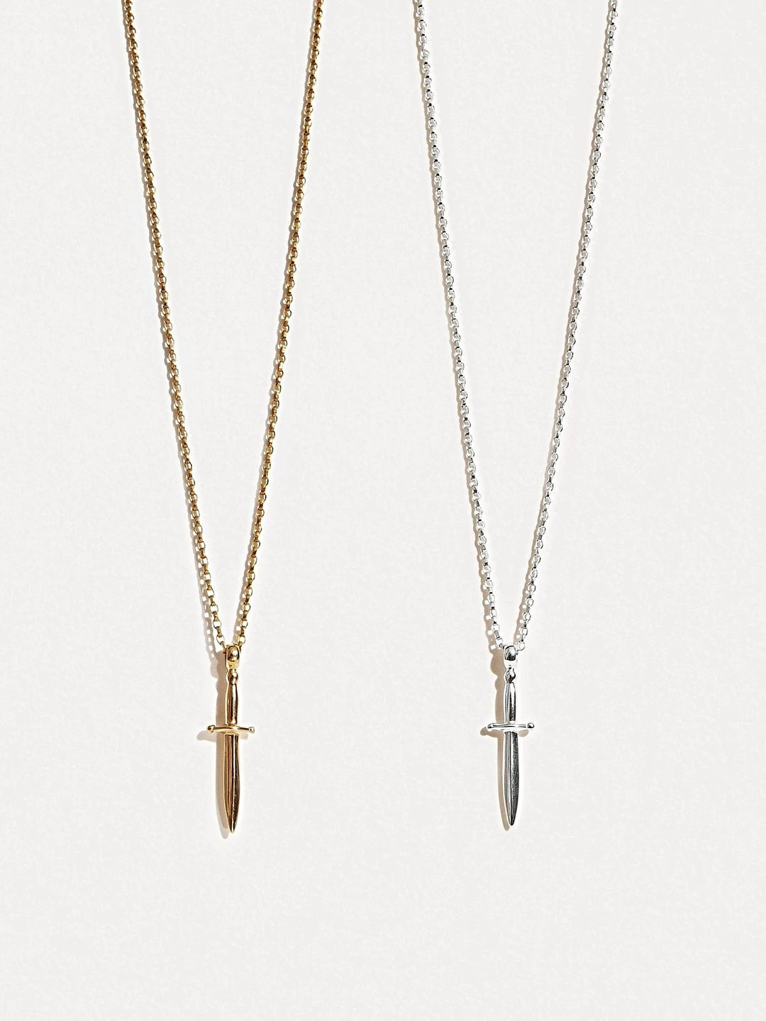 Gold and silver dagger necklaces side by side, showing both finish options.