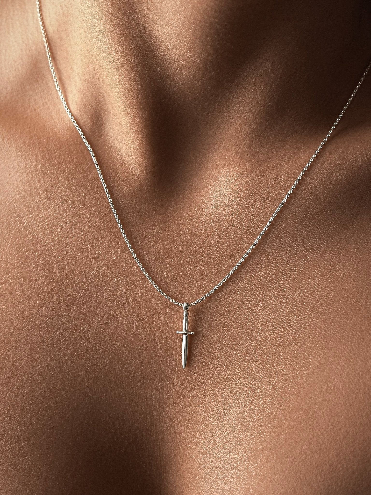 Sterling silver dagger necklace worn on bare skin, soft neckline, natural light.