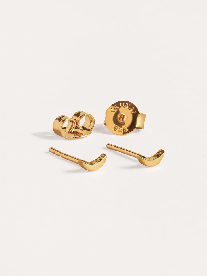 Gold crescent stud earrings worn individually, close-up on lobe