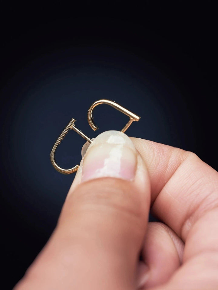 Close-up of Sita gold earring held between fingers — lightweight and modern bar design.