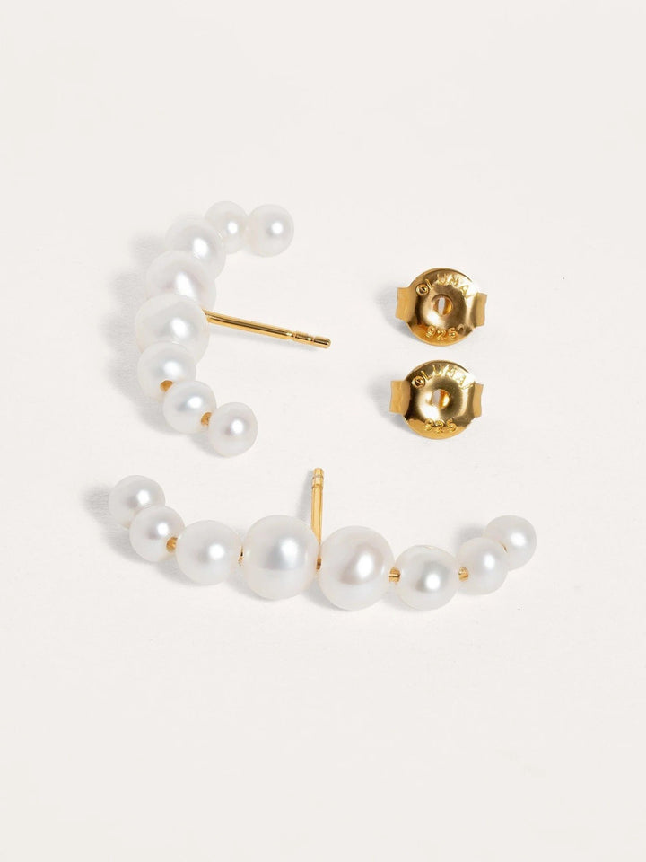 Close-up of a single gold-plated ear cuff with pearl detail, showcasing handcrafted design on a soft surface.