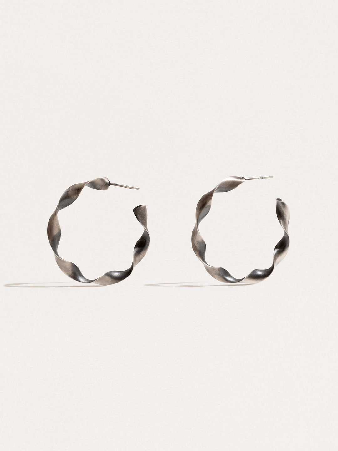 "Gene Twisted Hoop Earrings in silver oxide on neutral background"