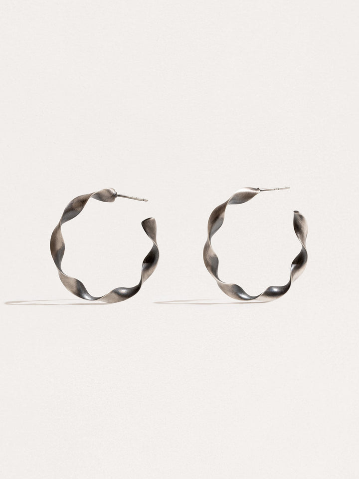 "Gene Twisted Hoop Earrings in silver oxide on neutral background"
