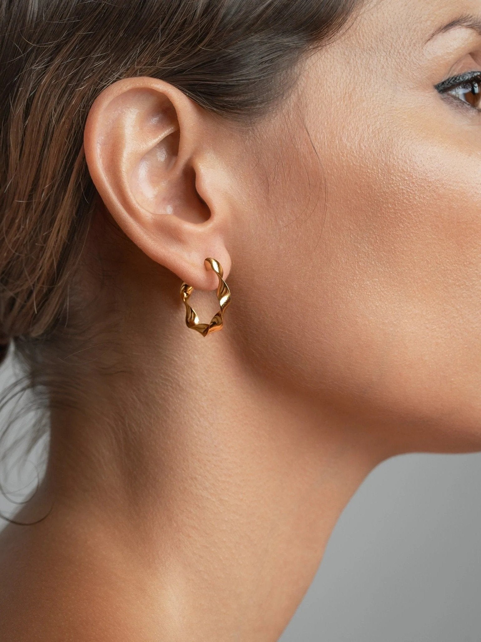 "Model wearing Gene Twisted Hoop Earrings in gold, side view"