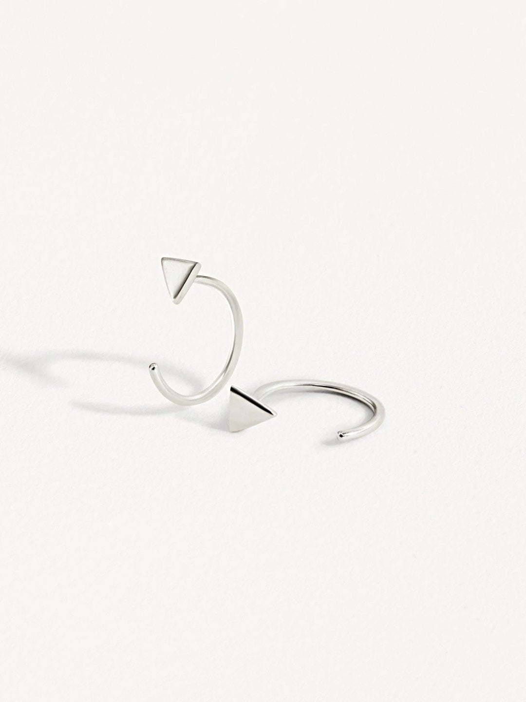 Pair of silver geometric triangle huggie earrings on white background