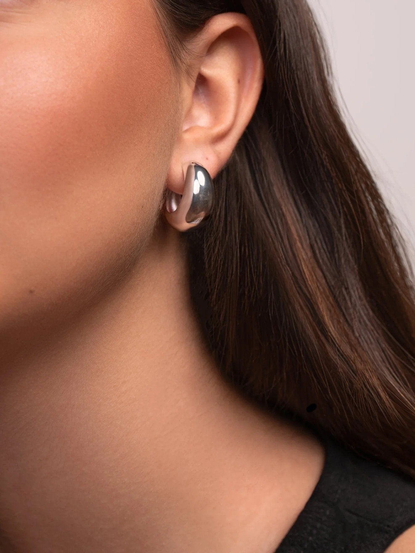 Close-up of a person wearing a silver hoop earring with a neutral background