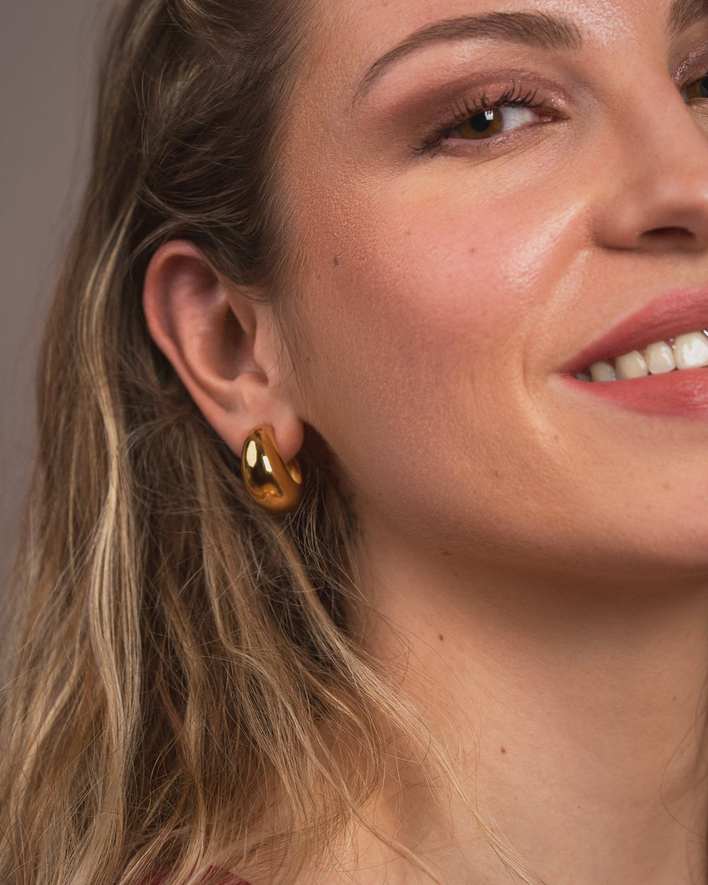 Close-up of a woman wearing gold earrings with a neutral background