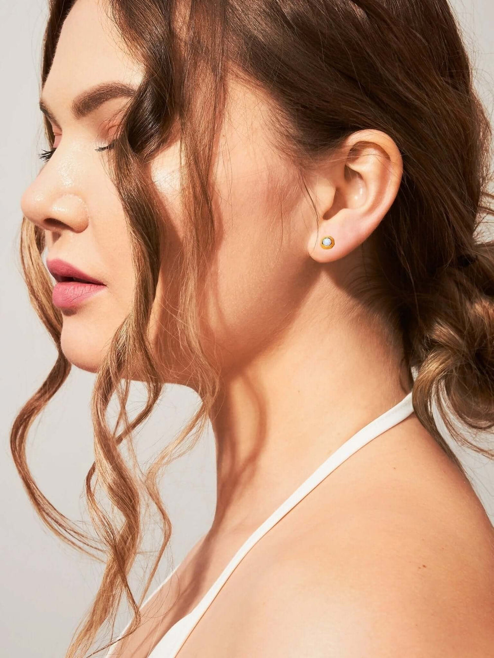 Close-up of model wearing gold stud earrings with natural gemstones.