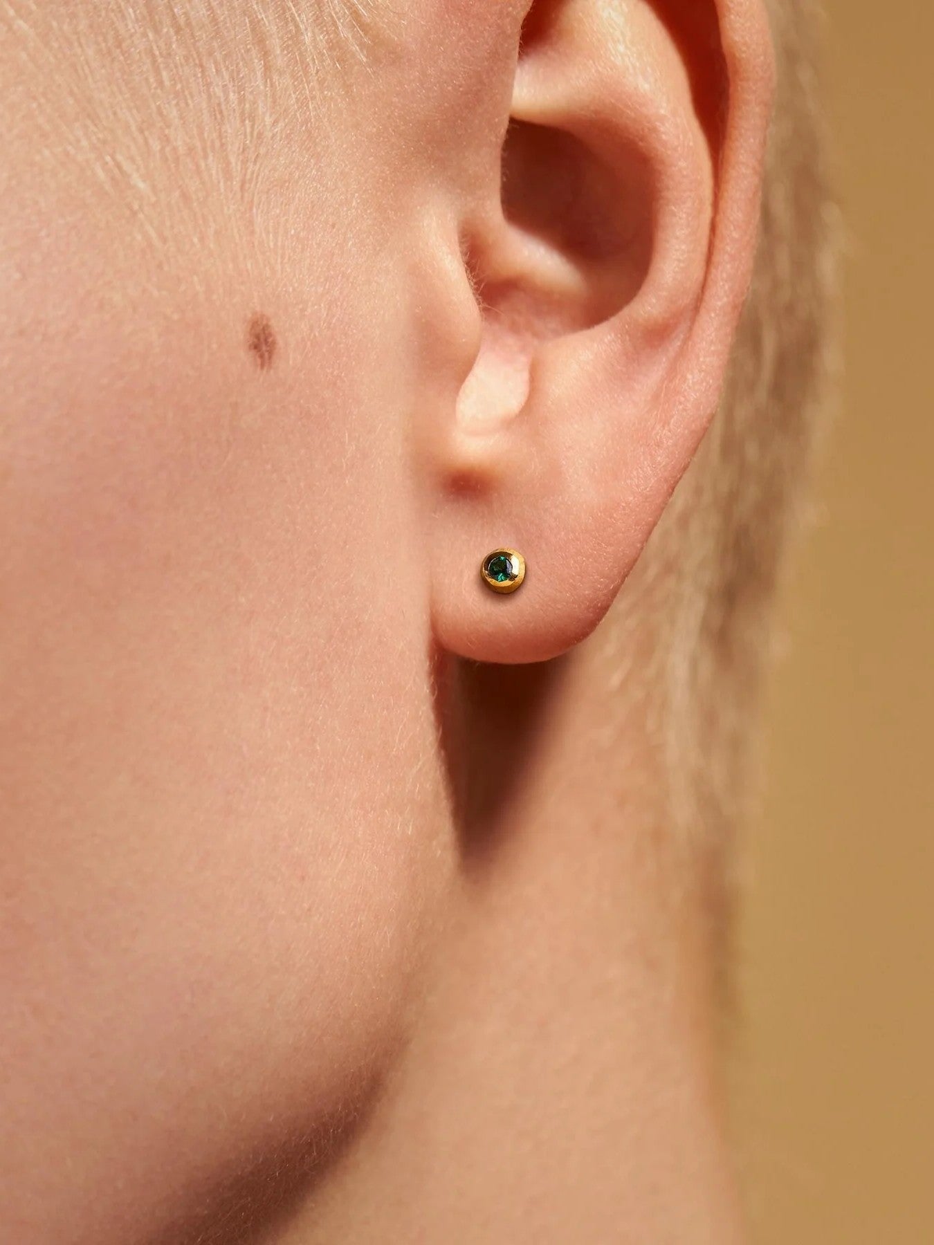 Gold stud earring with a green stone on a fair-skinned woman with short hair.