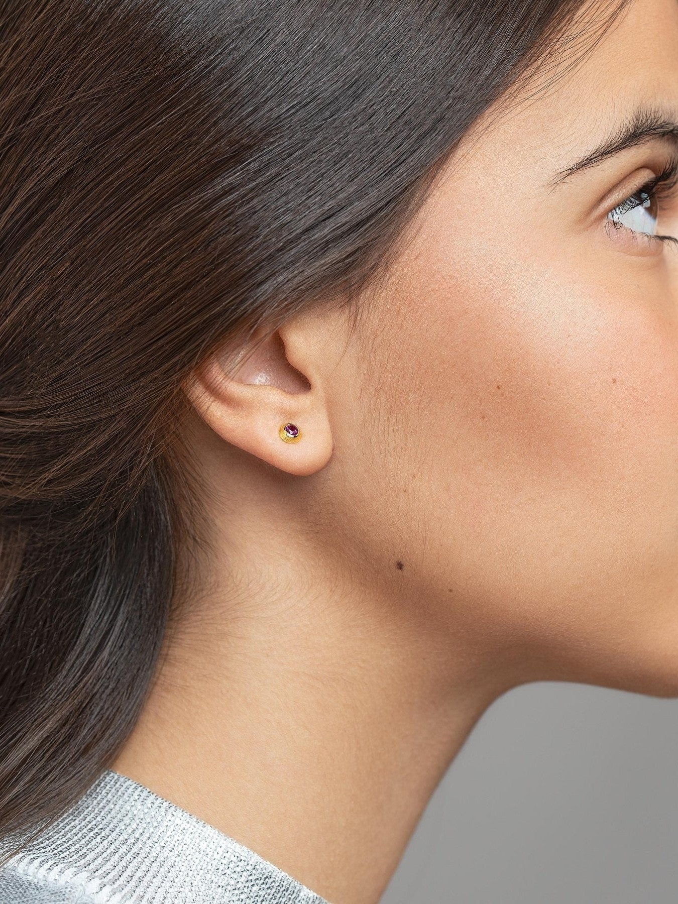 Side view of a woman with tied-back hair wearing a minimalist gold earring.