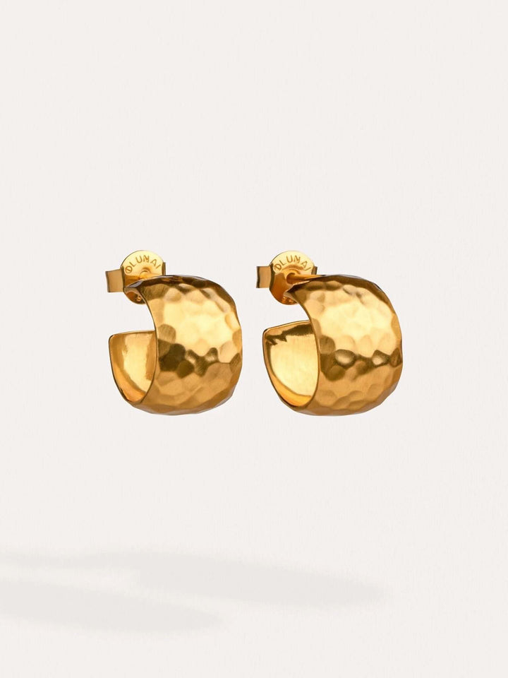 Gold hammered huggie hoops floating on a neutral background.