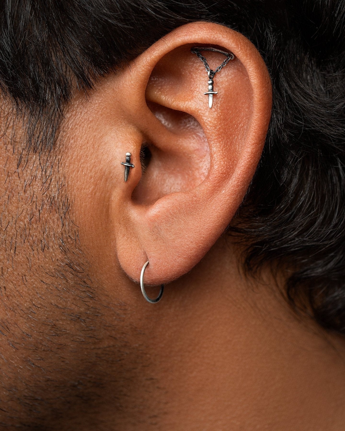 Back view of man's ear with dagger piercing in tragus