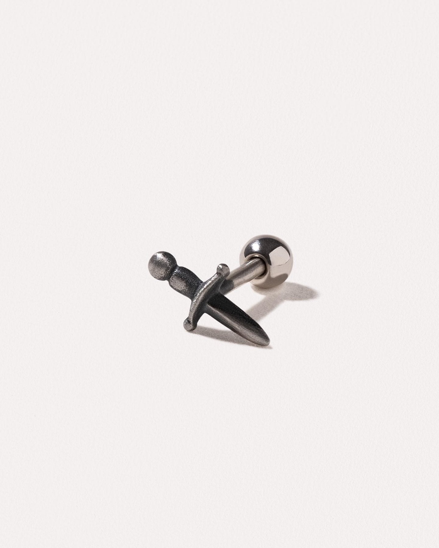 Close-up of oxidized silver dagger piercing on white background