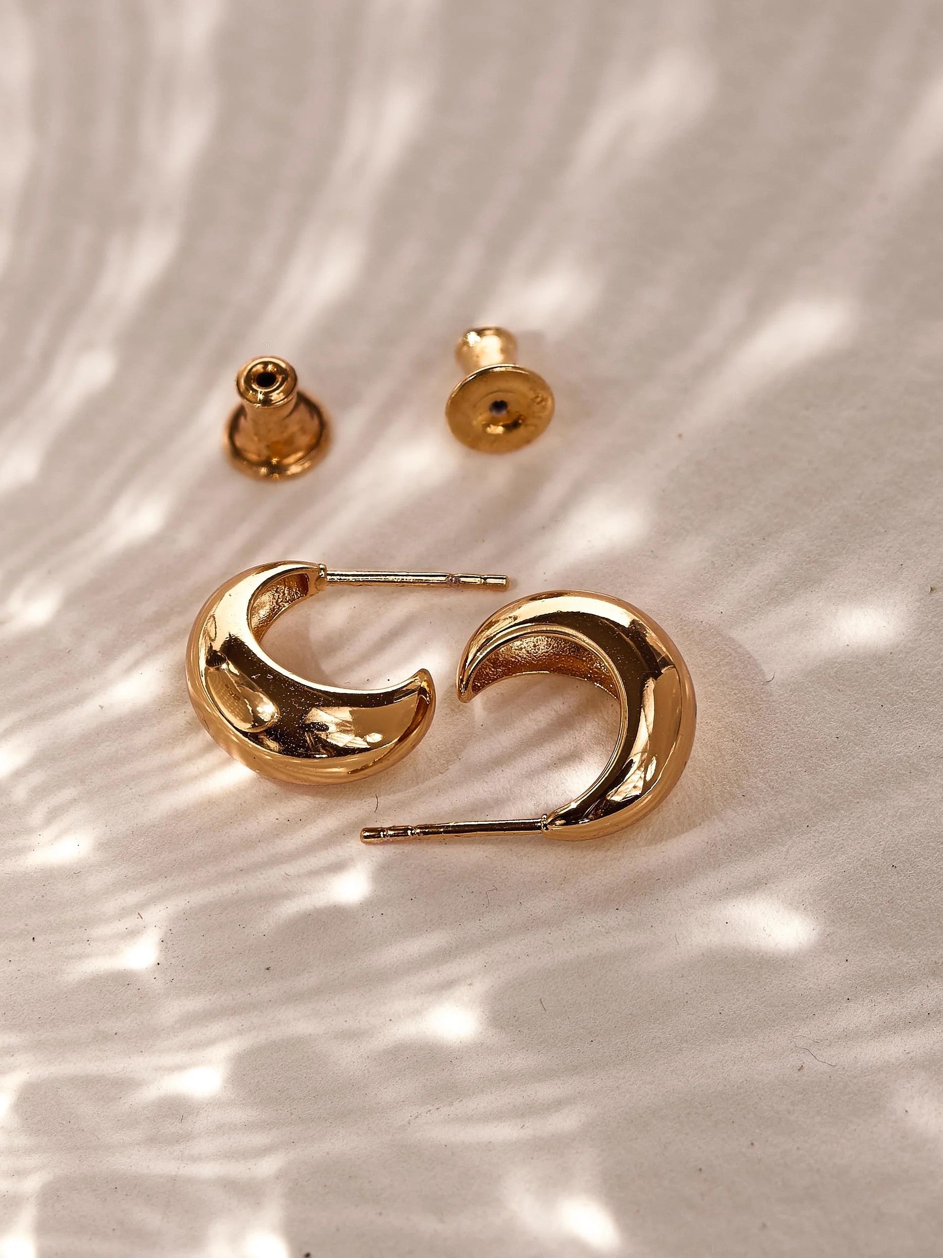 Close-up side view of small chunky gold crescent hoop earrings showing their rounded sculptural profile.