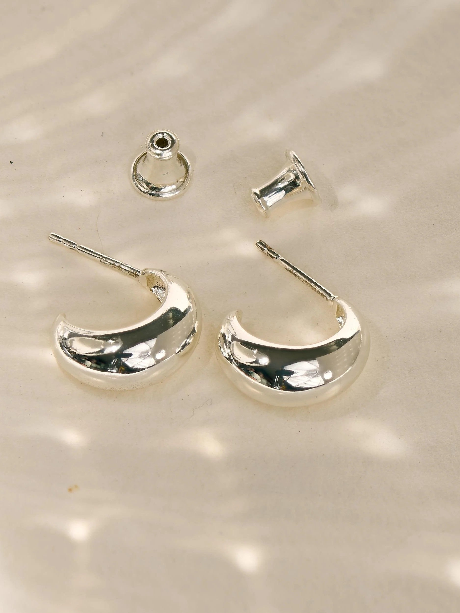 Silver plated crescent hoop earrings with matching backs, photographed on a softly textured neutral background.