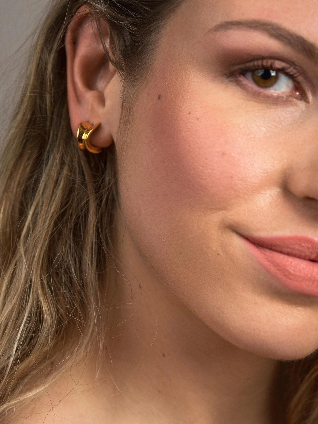 Close-up of woman wearing petite gold plated chunky hoops with a polished curved design.