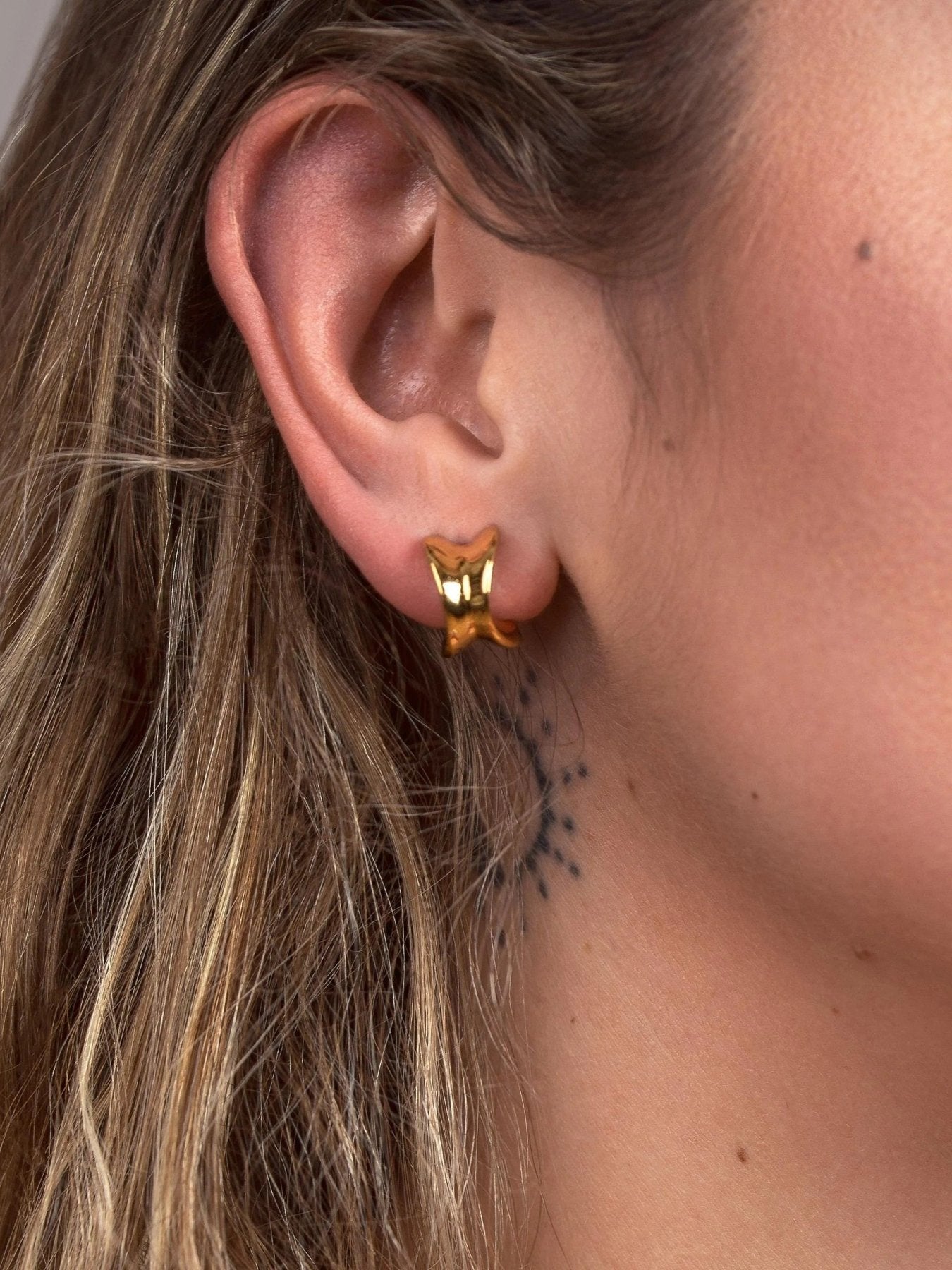 Side view of small gold chunky hoop earring worn close to the earlobe, showing its compact proportions.
