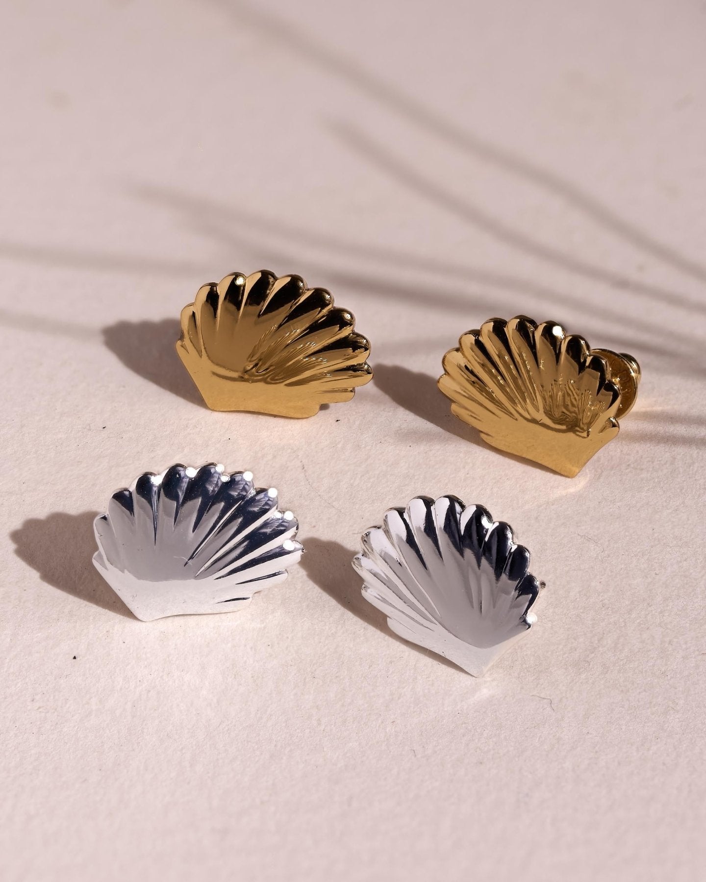 Gold and silver scallop shell stud earrings arranged together to compare the two available finishes.