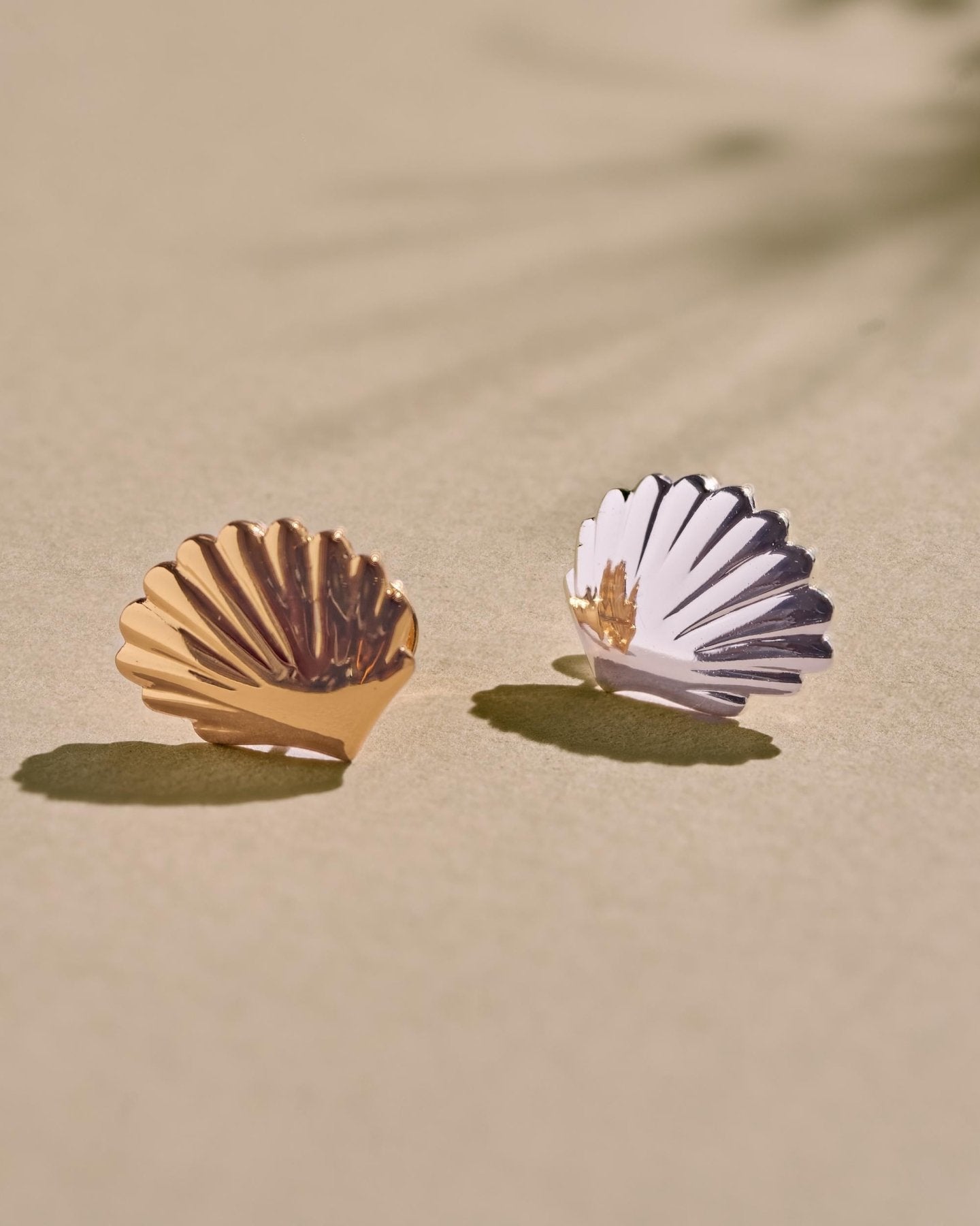 Gold and silver shell earrings shown side by side, highlighting the sculptural shape and contrasting finishes.