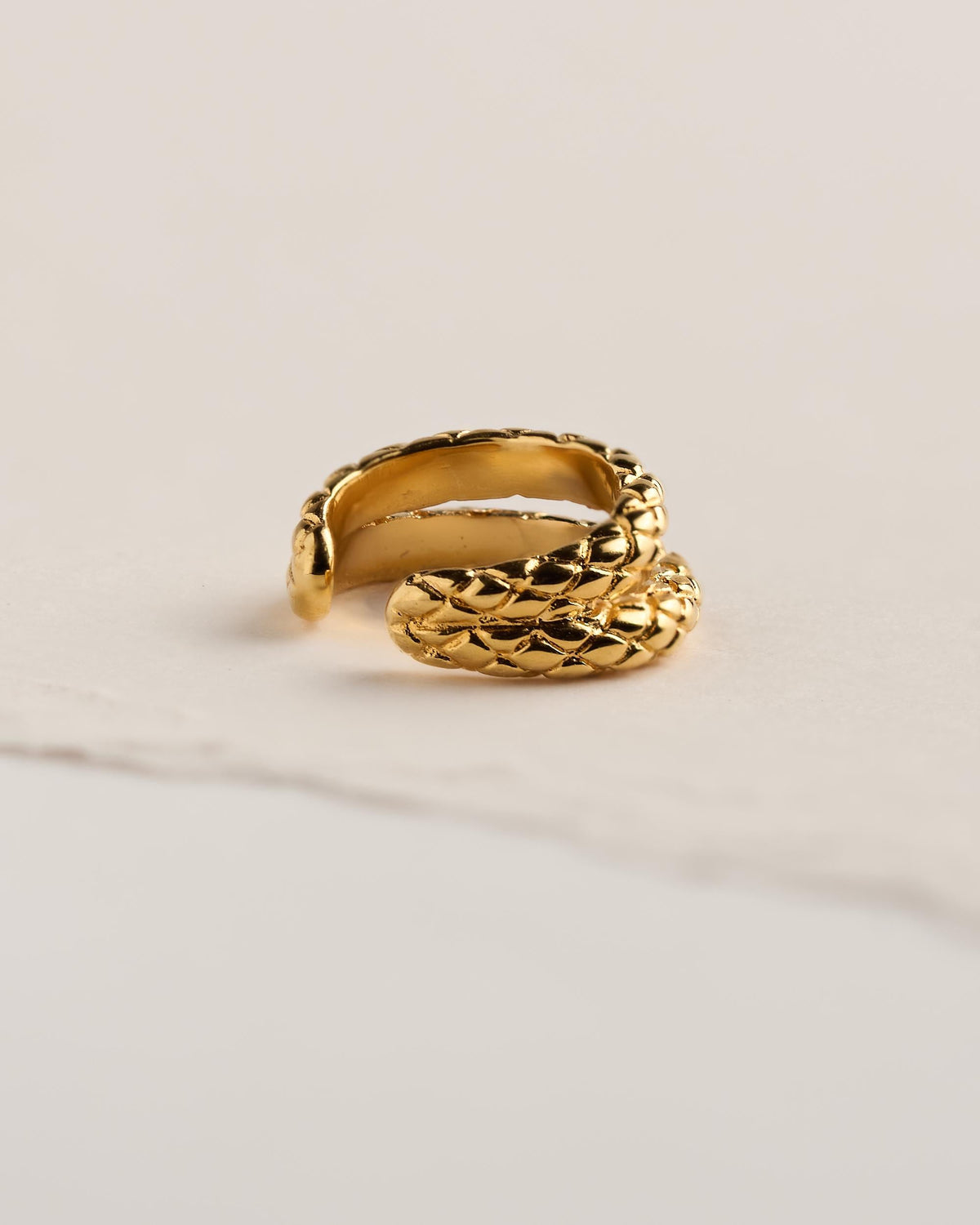 Side view of a 24k gold plated brass snake ear cuff showing its smooth inner band and the scale-textured snake head at the open end.