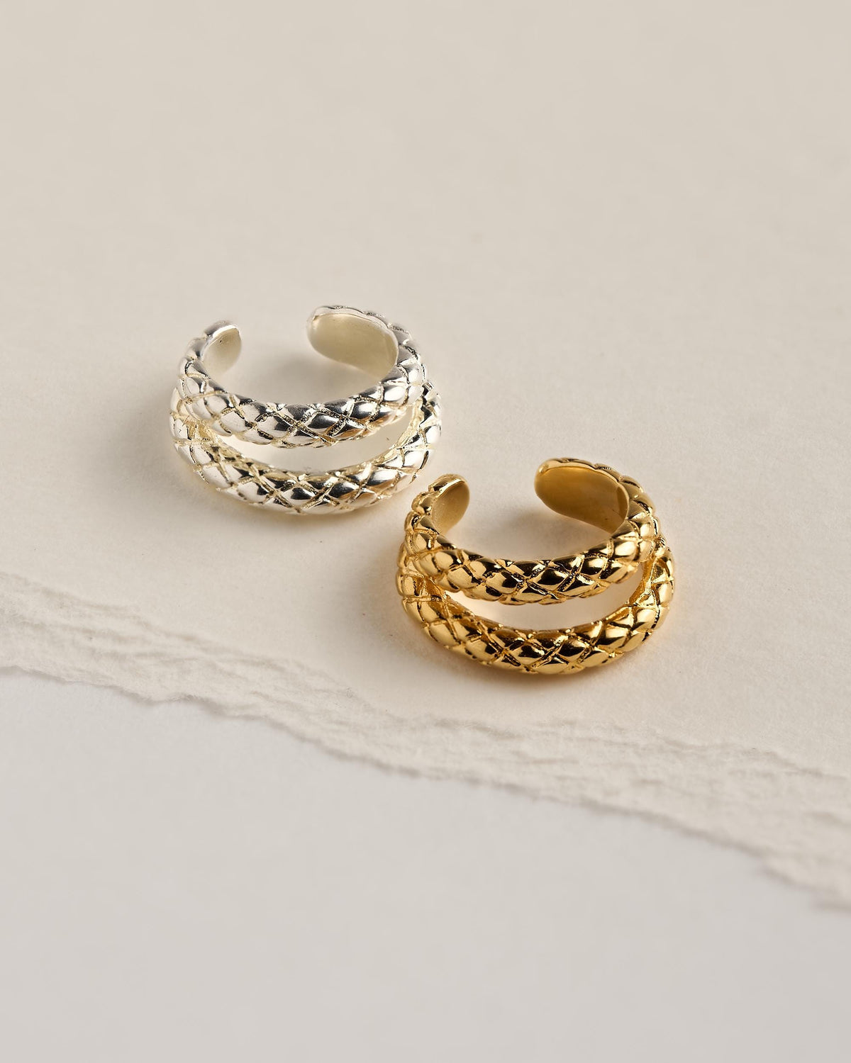 Two snake ear cuffs side by side, one in sterling silver plated brass and one in 24k gold plated brass, with engraved scale texture