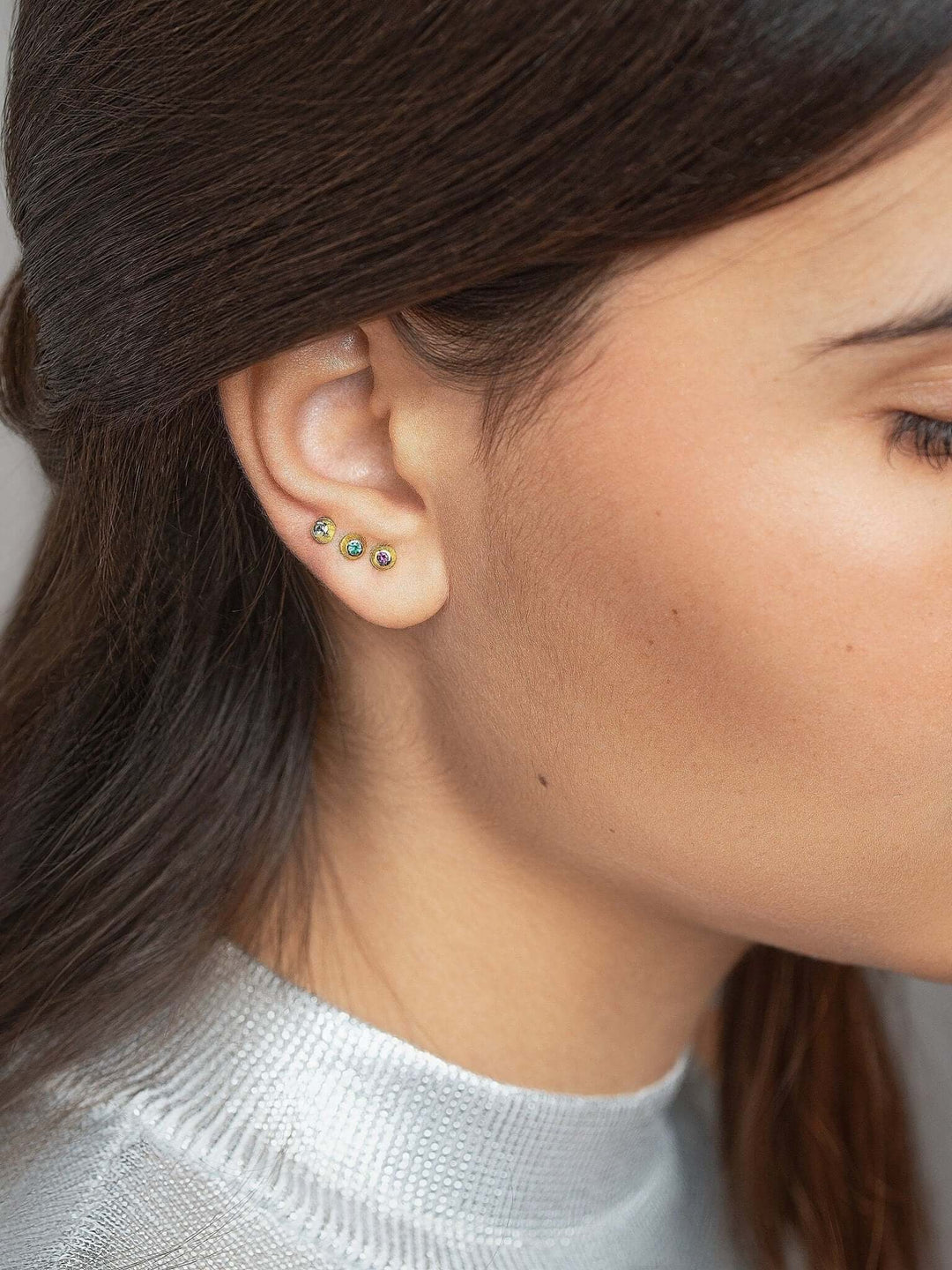 Elegant gold stud earrings worn with a sophisticated white blouse.