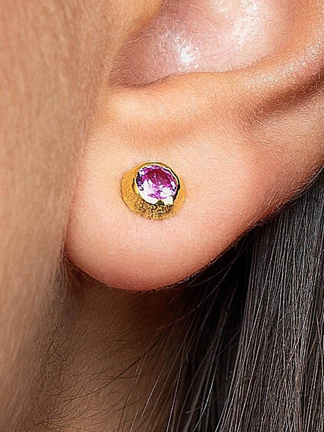 Close-up of pink stone earring on ear – gold stud earring with a pink gemstone, detailed view on skin.