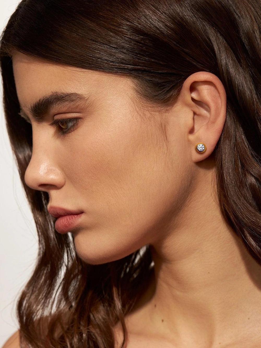 Woman wearing gold earrings with a white stone – model with loose hair showcasing gold and gemstone earrings.